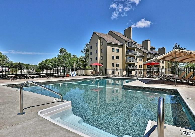 Outdoor swimming pool area with lounge chairs and a multi-story lodge building behind it.