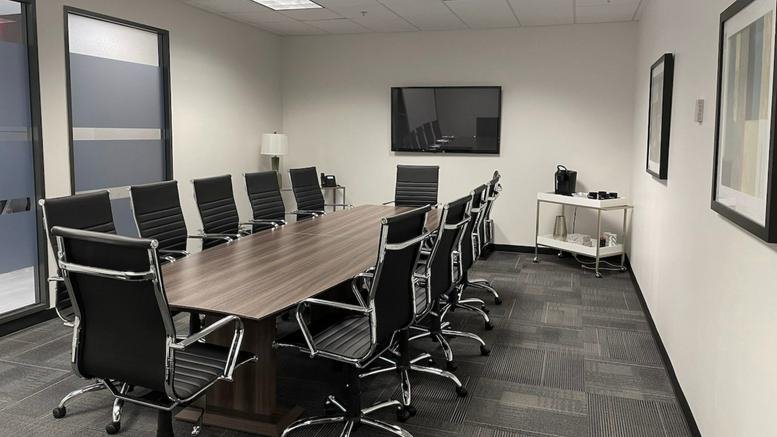 Spacious boardroom with a large wall-mounted monitor and grey carpeting.