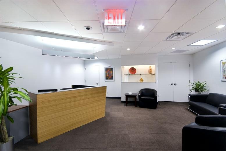 Bright reception area at 1350 Avenue of the Americas with a wooden front desk and green plants.