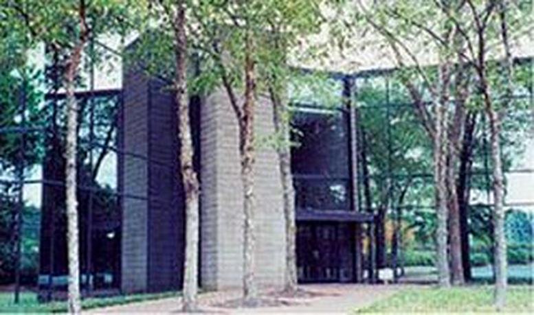 Modern glass and brick exterior of the 1355B Lynnfield Road office building surrounded by lush trees.