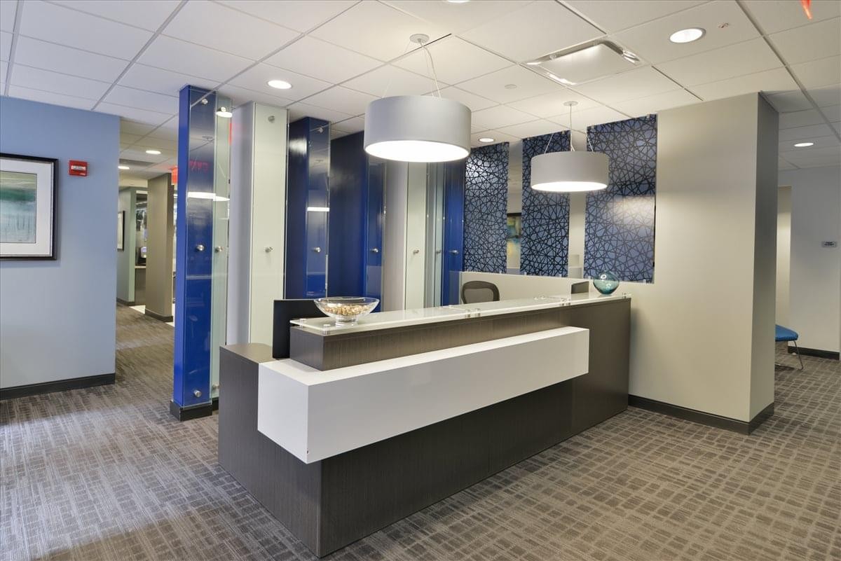 Modern reception desk with a white front panel, blue glass partitions, and large pendant lights.