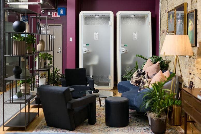 Lounge area at 140 Yonge Street with dark armchairs, a blue sofa, and white soundproof phone booths.