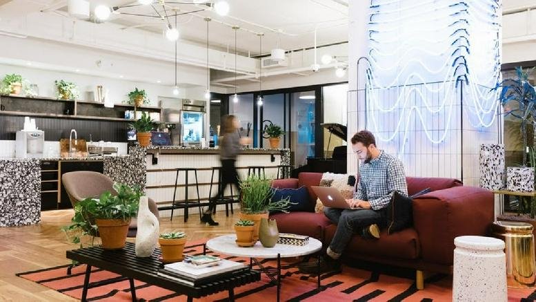 Spacious communal lounge with a red sofa, coffee tables, and plants at 142 W 57th Street.