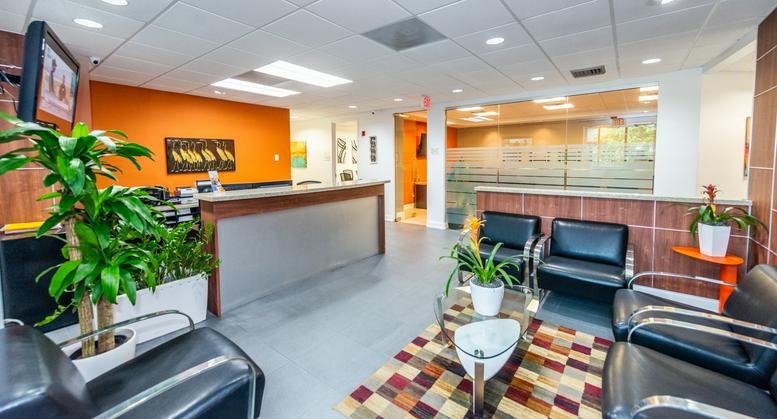 Modern reception area at 1451 West Cypress Creek Road, Suite 300, featuring an orange accent wall and potted plants.