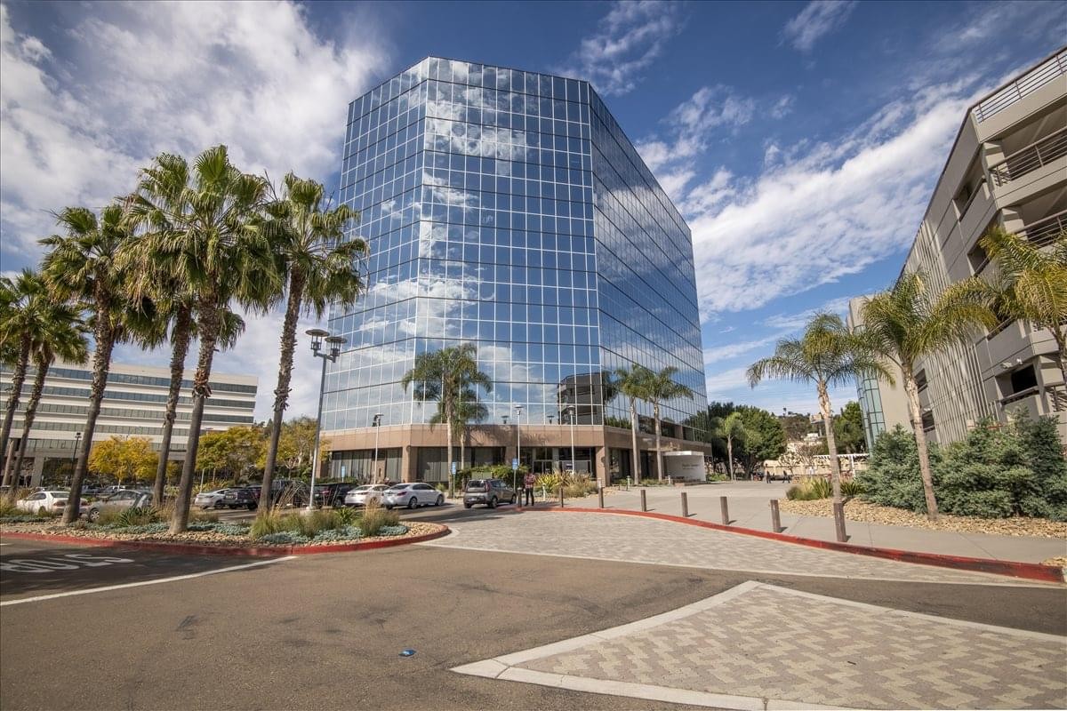 Exterior view of the glass-facade 1455 Frazee Road building with palm trees and blue sky.