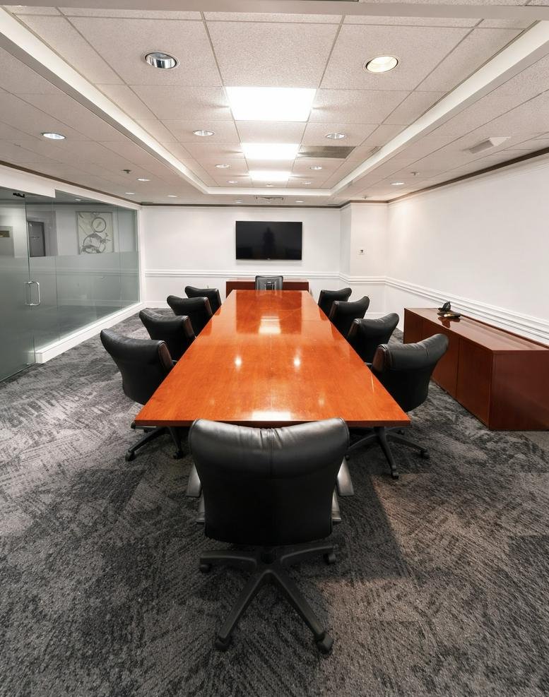 Spacious boardroom with a long polished wood table, black leather chairs, and recessed ceiling lighting.