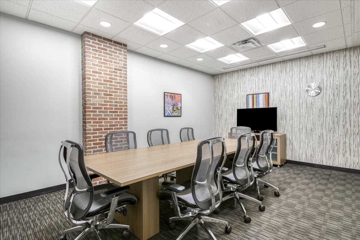 Professional boardroom at Raintree Corporate Center featuring a long wooden table and brick accent wall.