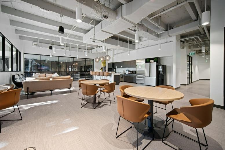 Expansive communal kitchen and lounge area with warm tan seating and industrial ceilings.