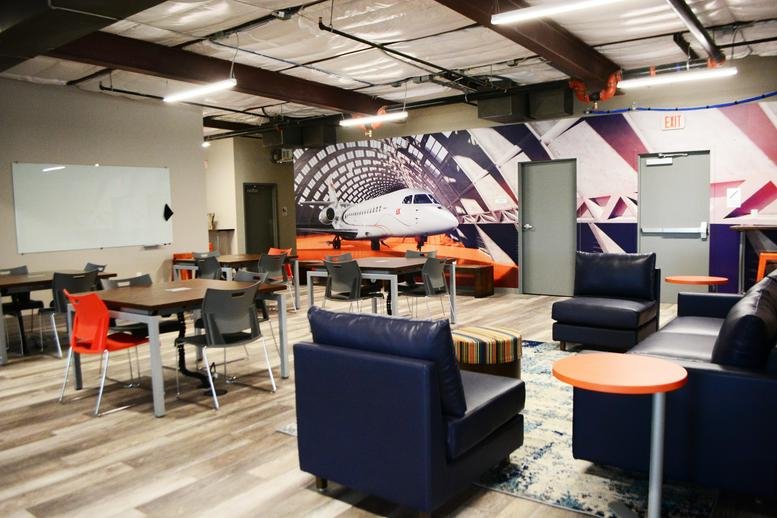 Spacious communal workspace at 15492 Voss Road with navy lounge chairs and airplane wall art.