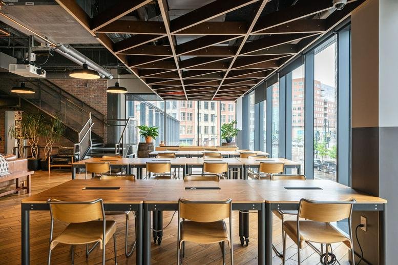 Large open-plan coworking area with long wooden tables and a geometric timber ceiling installation.