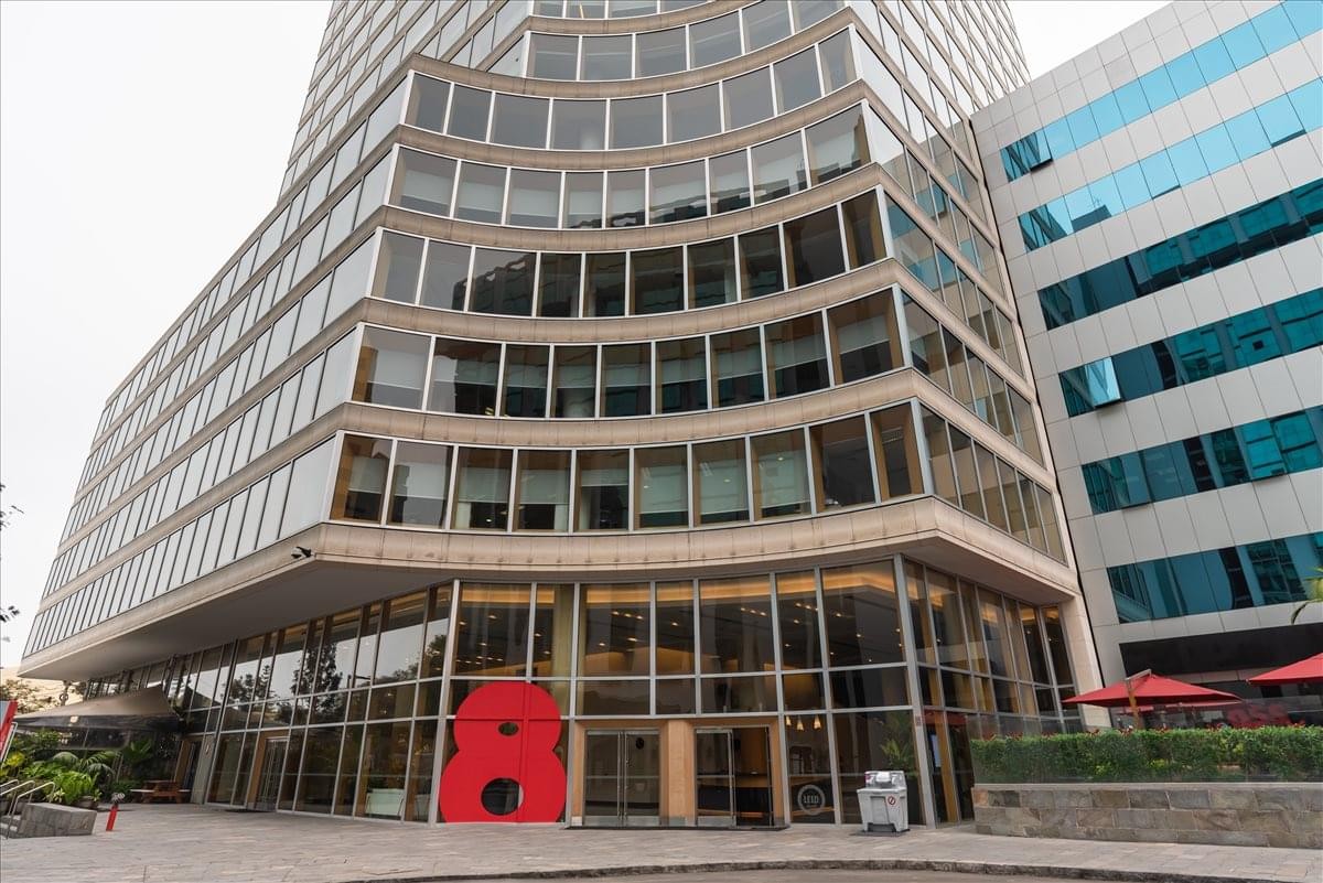 Exterior view of the curved glass-facade 16th Floor Real Ocho Building with a red sculpture at the entrance.