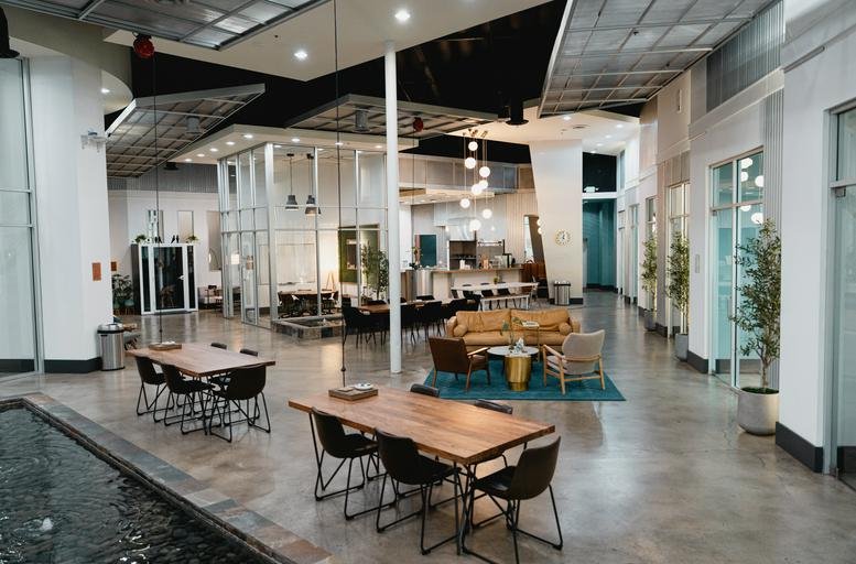 Spacious open-plan communal area at WorkWell OC with modern seating, wooden tables, and a water feature.