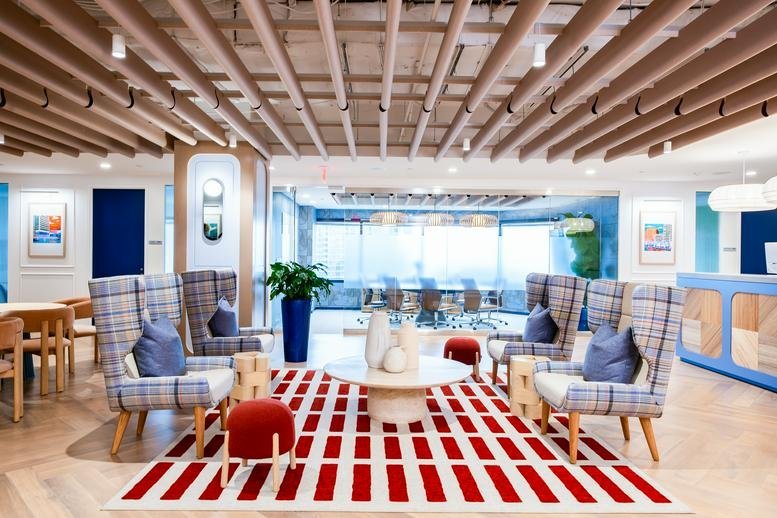 Bright communal lounge with plaid armchairs, a red patterned rug, and a wood-slat ceiling.