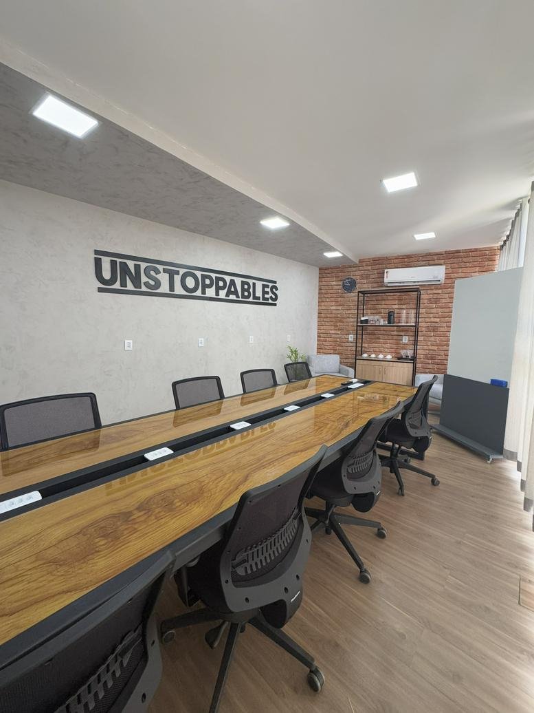 Spacious boardroom with a long wooden table, black mesh chairs, and Unstoppables wall branding.