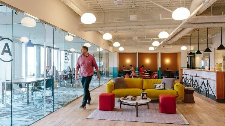 Large lounge at 2 Embarcadero Center with a yellow sofa, red ottomans, and views of office pods.