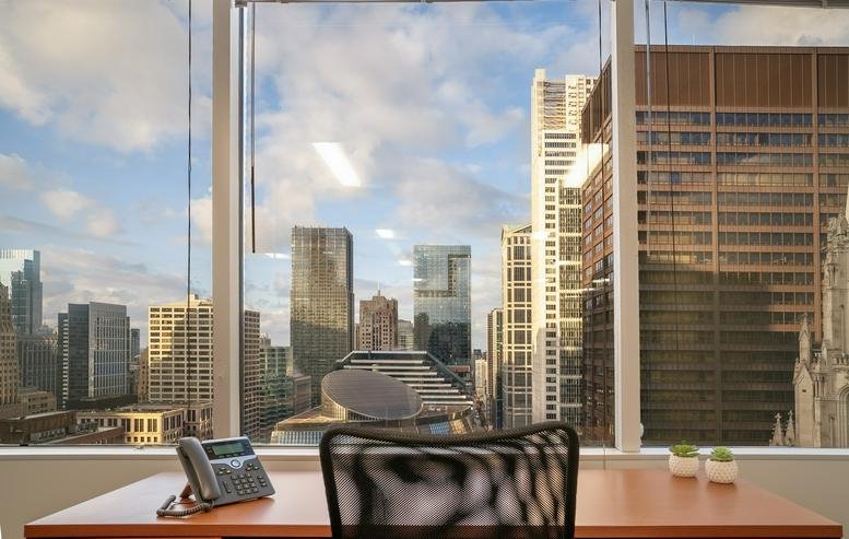 Cityscape view from an office window with a desk and phone.