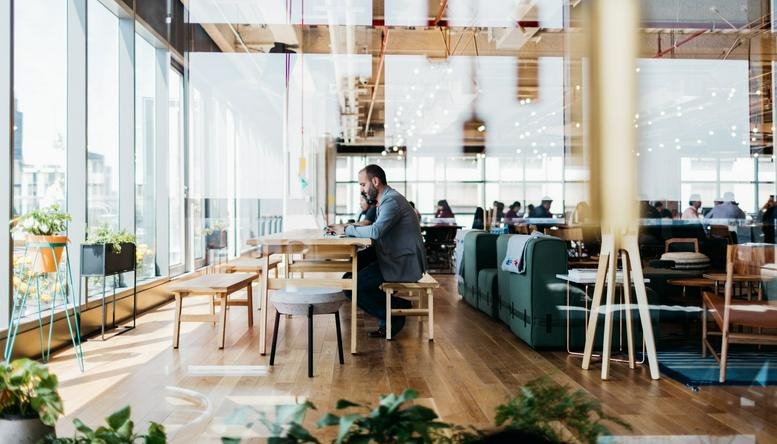 Spacious, sun-drenched coworking lounge at 201 Spear Street with wood floors and green velvet sofas.