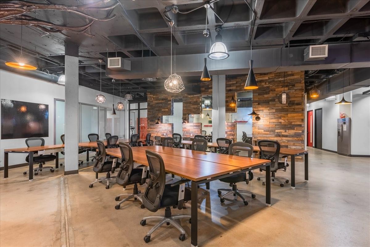 Coworking area at 2021 Guadalupe Street with long wooden desks and industrial ceilings.