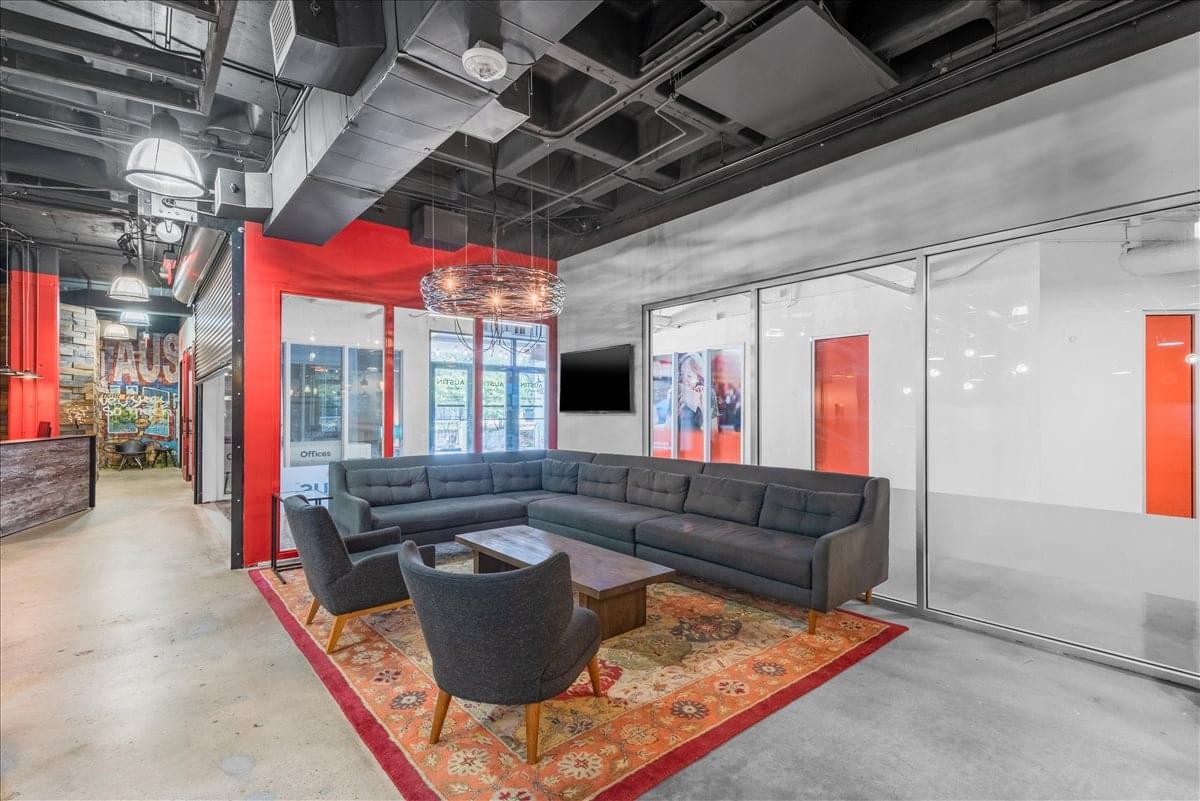 Modern lounge area at 2021 Guadalupe Street with an L-shaped sofa and glass-walled meeting rooms.