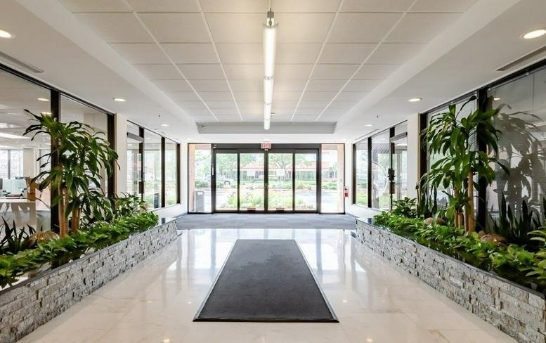 Lobby at 2021 Midwest Road, Suite 200, with bright white flooring, stone planters, and lush greenery.