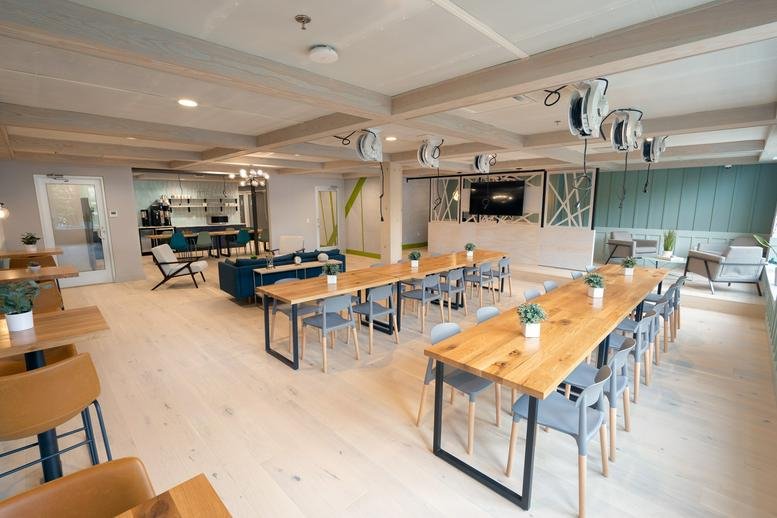 Large open-plan workspace with multiple rows of wooden communal tables and blue seating.