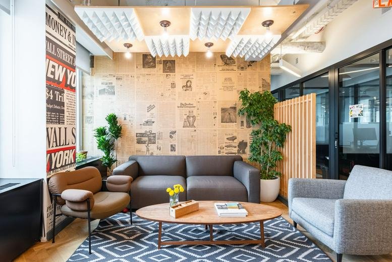 Bright lounge with newsprint wallpaper, grey sofa, and potted plants.