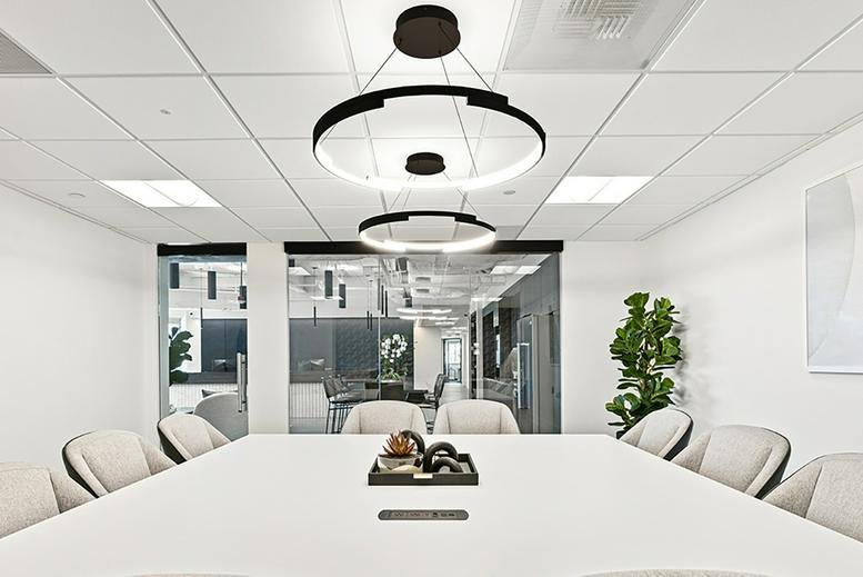 Meeting room with modern ring pendant lights and grey chairs around a large white table.