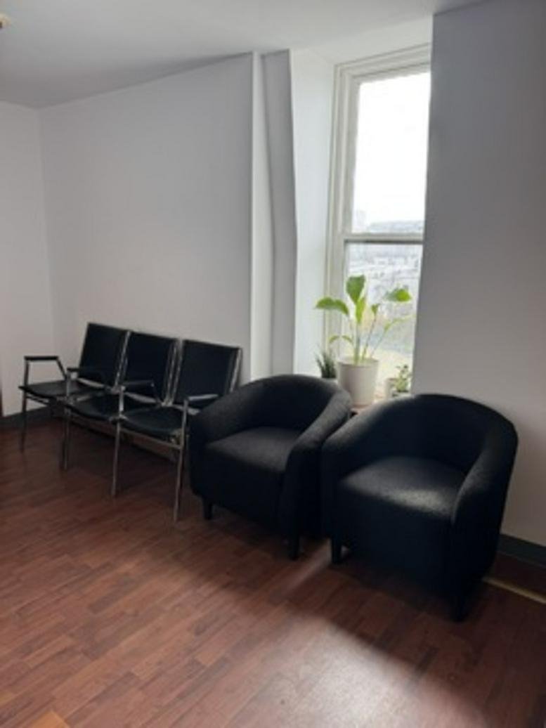 Waiting area at 247 Prospect Avenue, 4th Floor with black armchairs, metal seating, and a sunlit window with a plant.