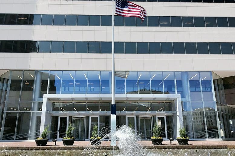 Building entrance with glass facade, American flag, and water fountain.