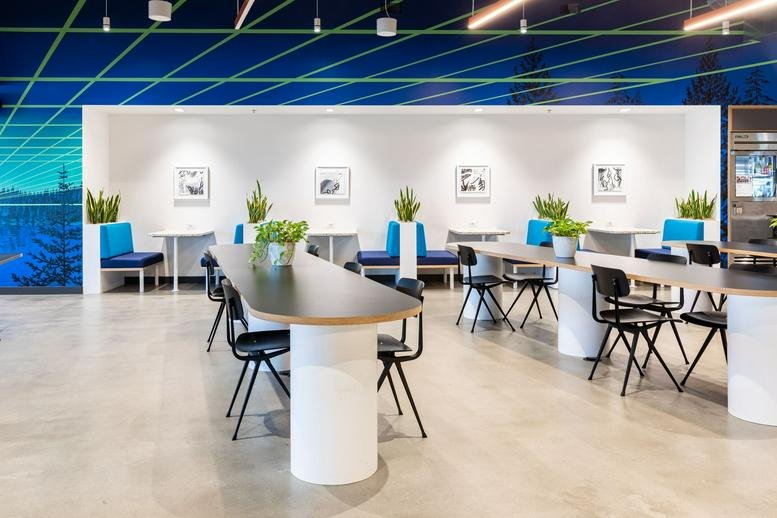 Spacious coworking area with long white tables and a blue mountain-themed feature wall.