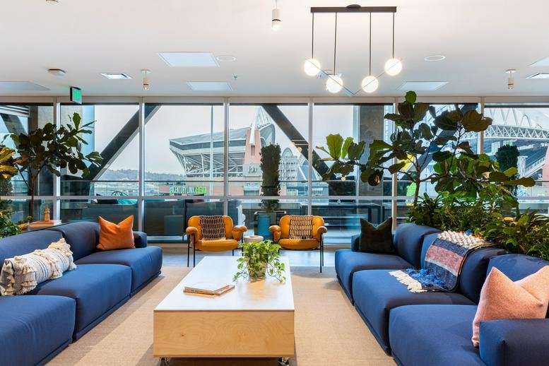 Lounge area with blue sectional sofas, orange armchairs, and floor-to-ceiling windows.