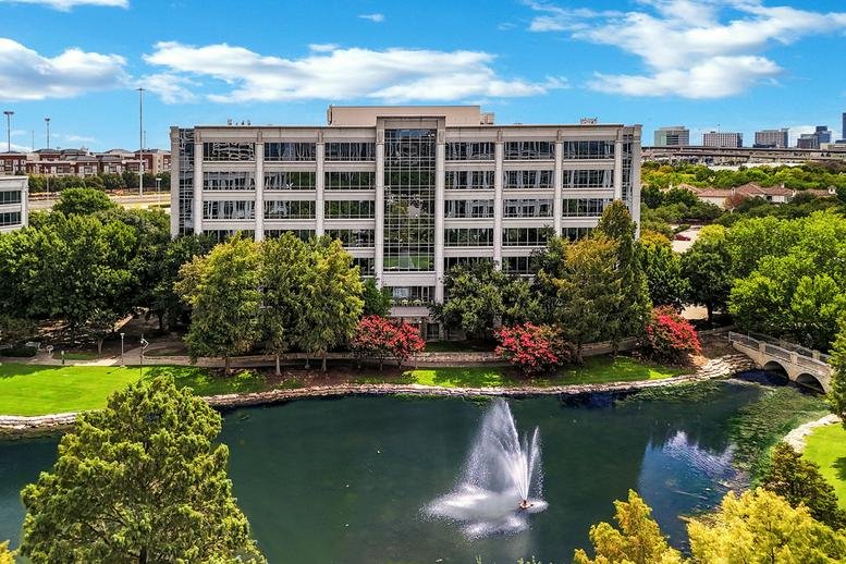 Exterior view of the office building at 2591 Dallas Parkway with a scenic pond and fountain in the foreground.