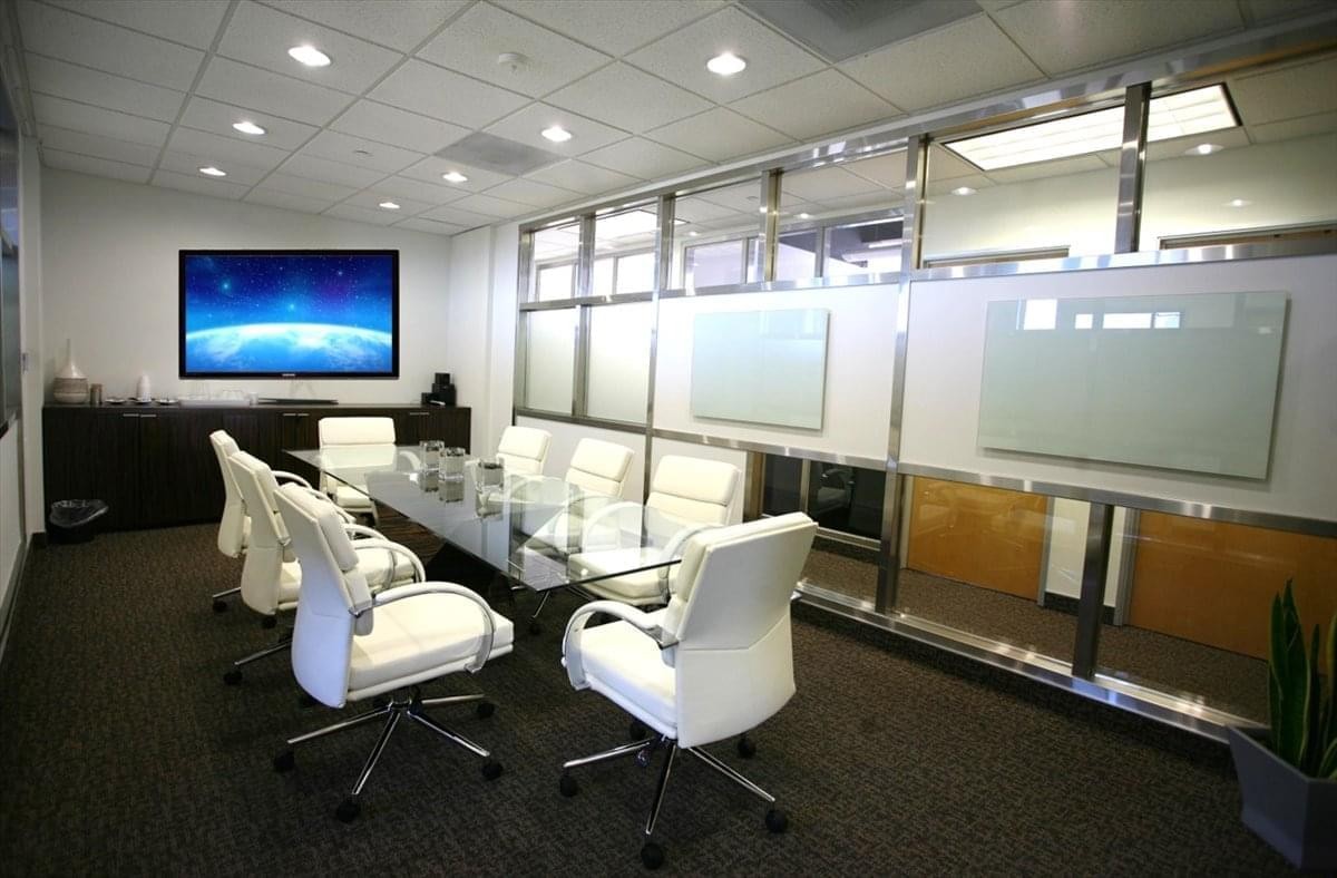 Meeting room at 260 Newport Center Drive, Suite 100 with white chairs and a large wall-mounted monitor.
