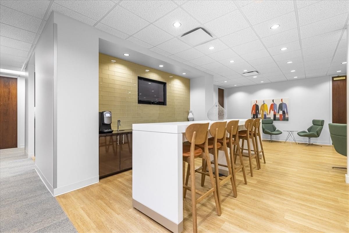Communal break area with a long white kitchen island, wooden bar stools, and lounge seating.