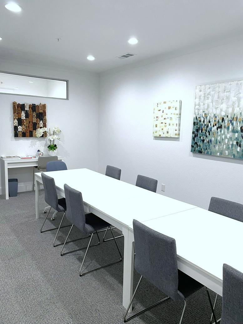 Meeting room with a long white table, grey chairs, and abstract wall art.