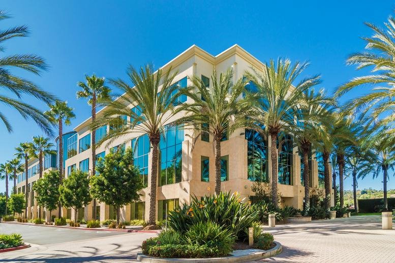 Exterior of the modern glass and stone building at 27201 Puerta Real, Suite 300, lined with palm trees.