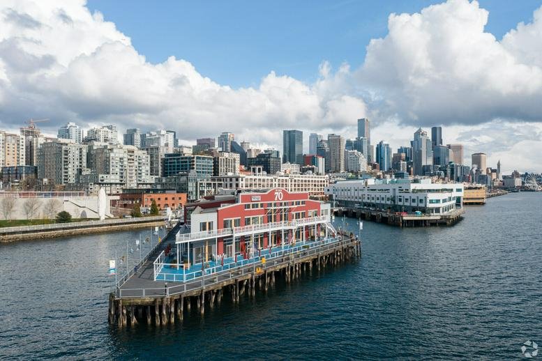 Dusk view of the red and white Pier 70 building on the Seattle waterfront with the city skyline behind it.