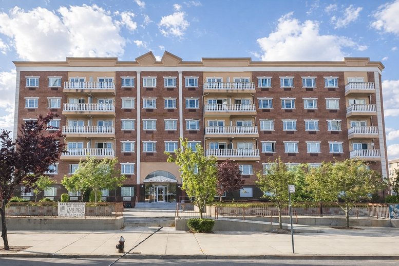 Close-up of the brick and tan facade of the Office on the Bay building with green trees in front.