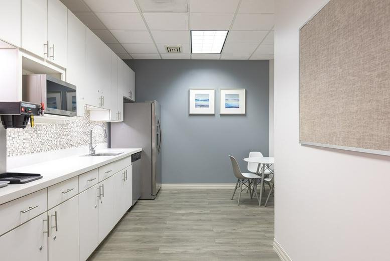 Modern communal kitchen area with white cabinetry and grey accent wall.