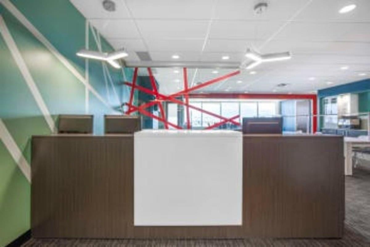 Modern reception desk at 3055 Saint Martin Ouest, T500 with a teal geometric feature wall and red art sculpture.