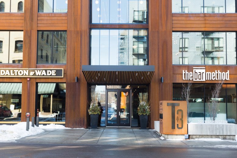 Exterior entrance of 323 Washington Avenue North featuring a weathered steel facade and wood accents.