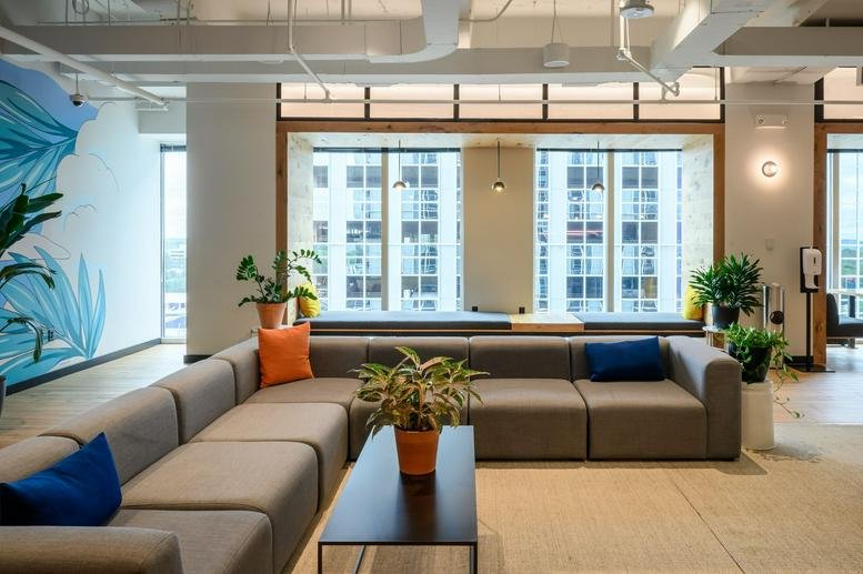Large lounge area with a grey sectional sofa, orange pillows, and floor-to-ceiling windows.