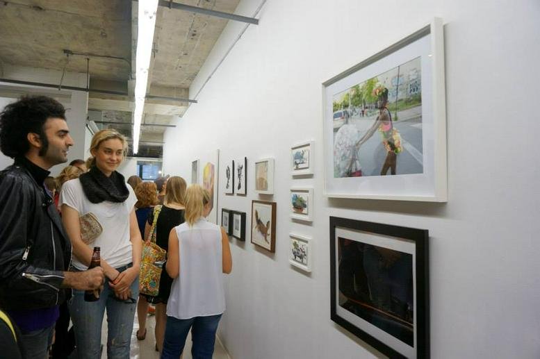 People attending an art gallery opening at 33 Nassau Avenue with framed photography on white walls.