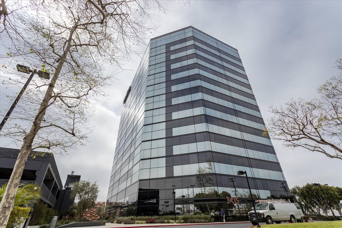Exterior view of the glass-facade 3415 South Sepulveda Blvd building under a bright sky.