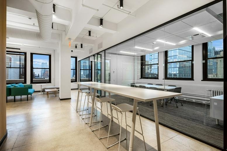 Long white high-top table with stools next to a glass-partitioned meeting room.