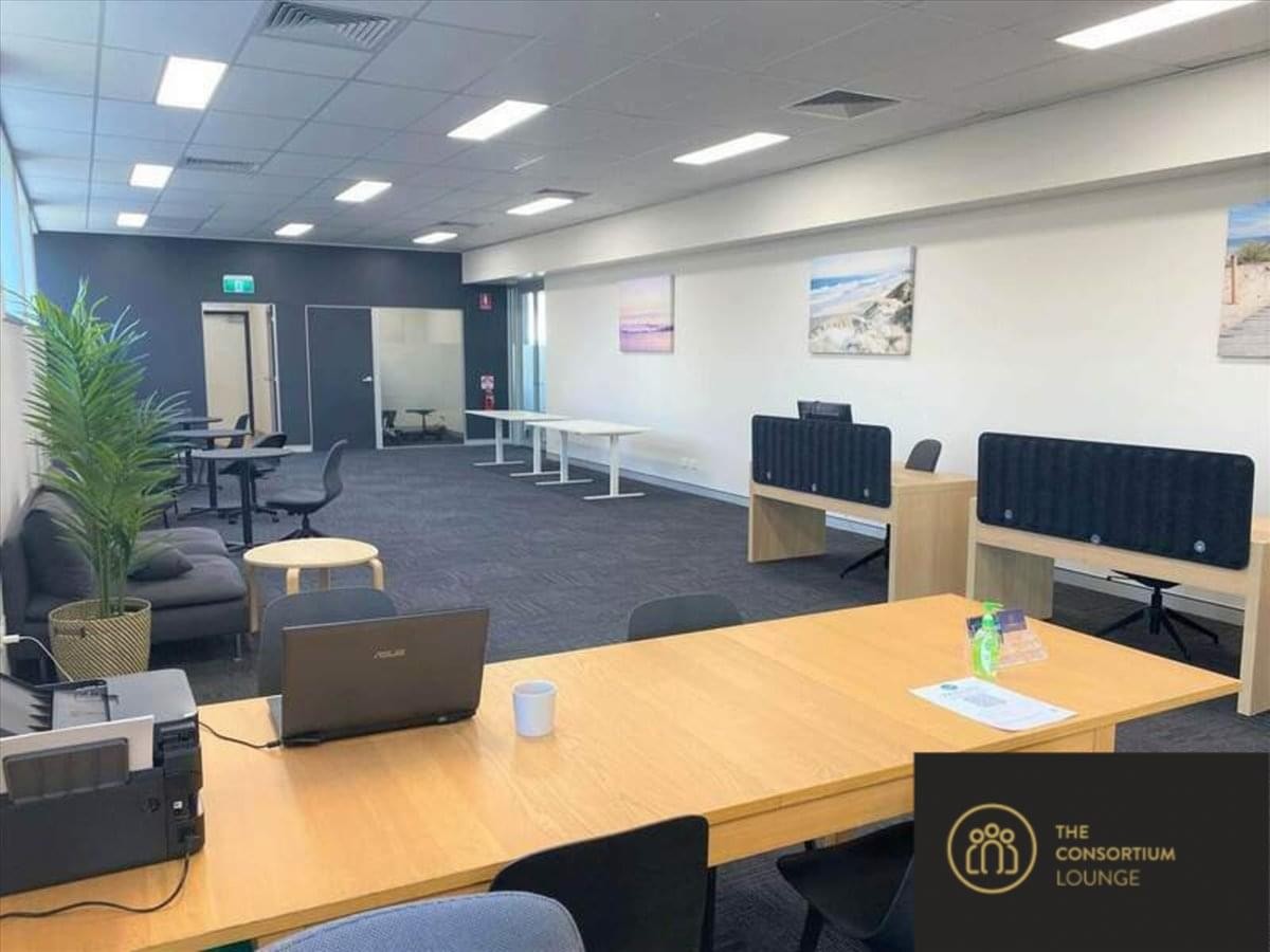 Spacious co-working lounge with wooden tables, a laptop, and indoor plants at Ferncroft Corporate Centre.