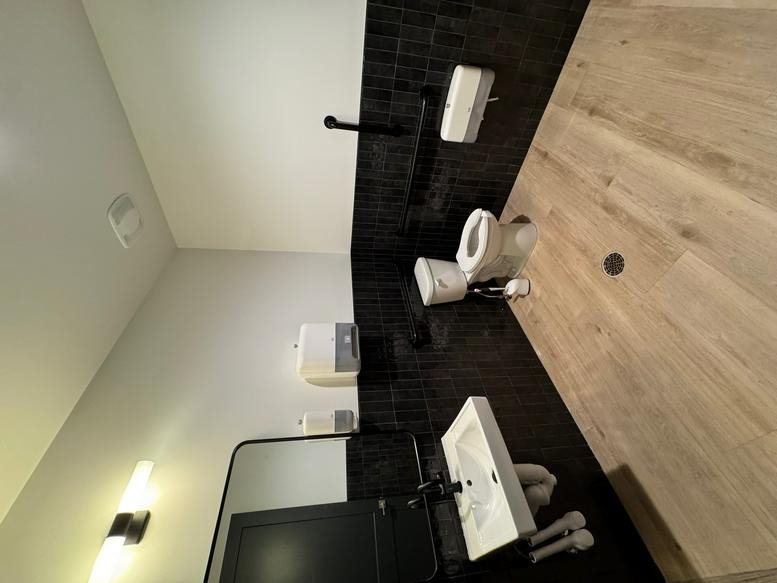 Modern restroom with dark tiling, white fixtures, and wood-look flooring.