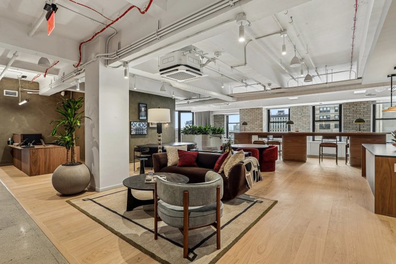 Spacious communal lounge at 386 Park Avenue South with modern furniture, a large plant, and high industrial ceilings.