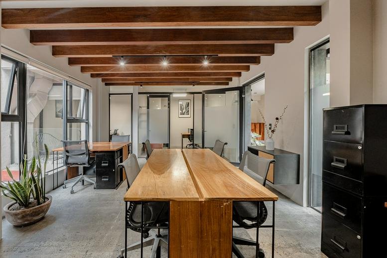 Spacious office suite with warm wooden ceiling beams and shared workstations.