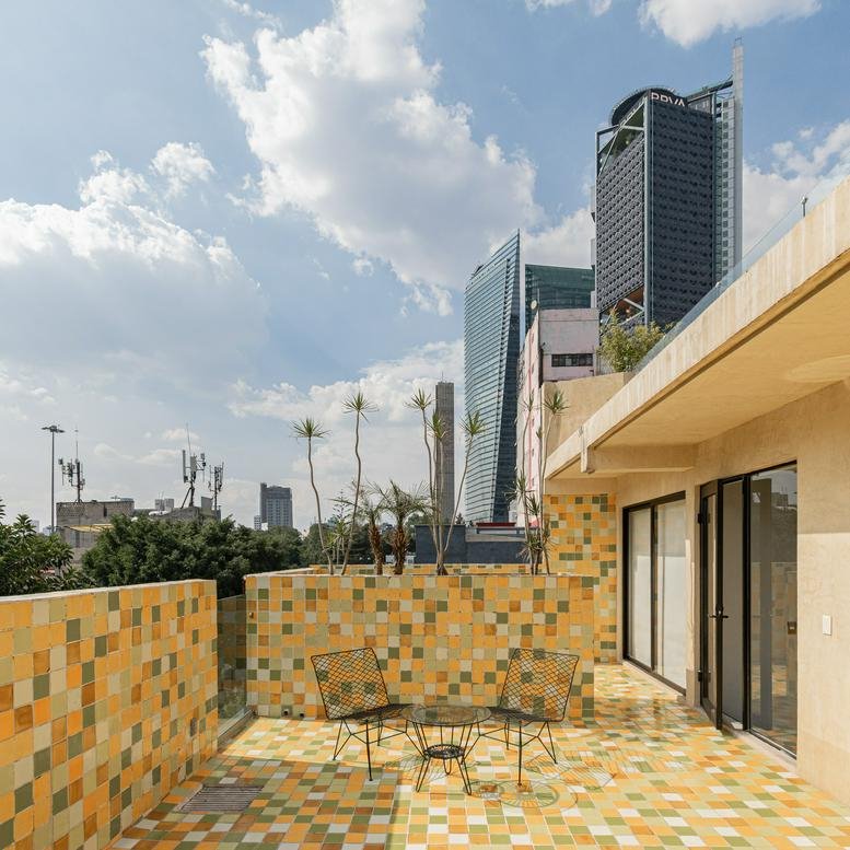 Sun-drenched rooftop terrace with vibrant patterned floor tiles and city skyline views.